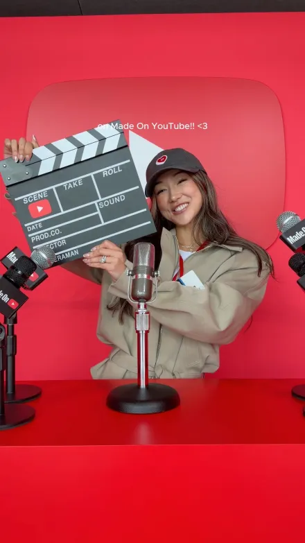 Vanessa Lau short-form post: a woman in a cap holding a clapperboard in front of a red backdrop at a YouTube event.