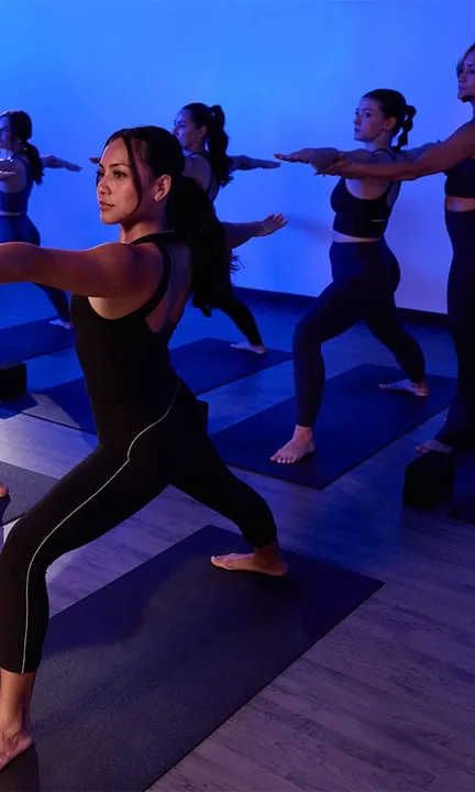 YogaSix short-form post: women in a warrior pose on mats in a blue-lit studio.