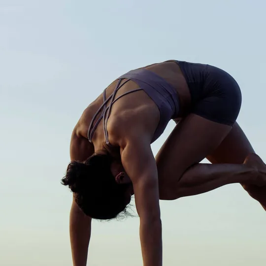 YogaWorks short-form post: a person folded forward in a crouched yoga pose against a pale sky.